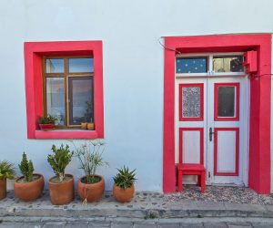 View of house with red door frame and window with potted plants in Bozcaada village